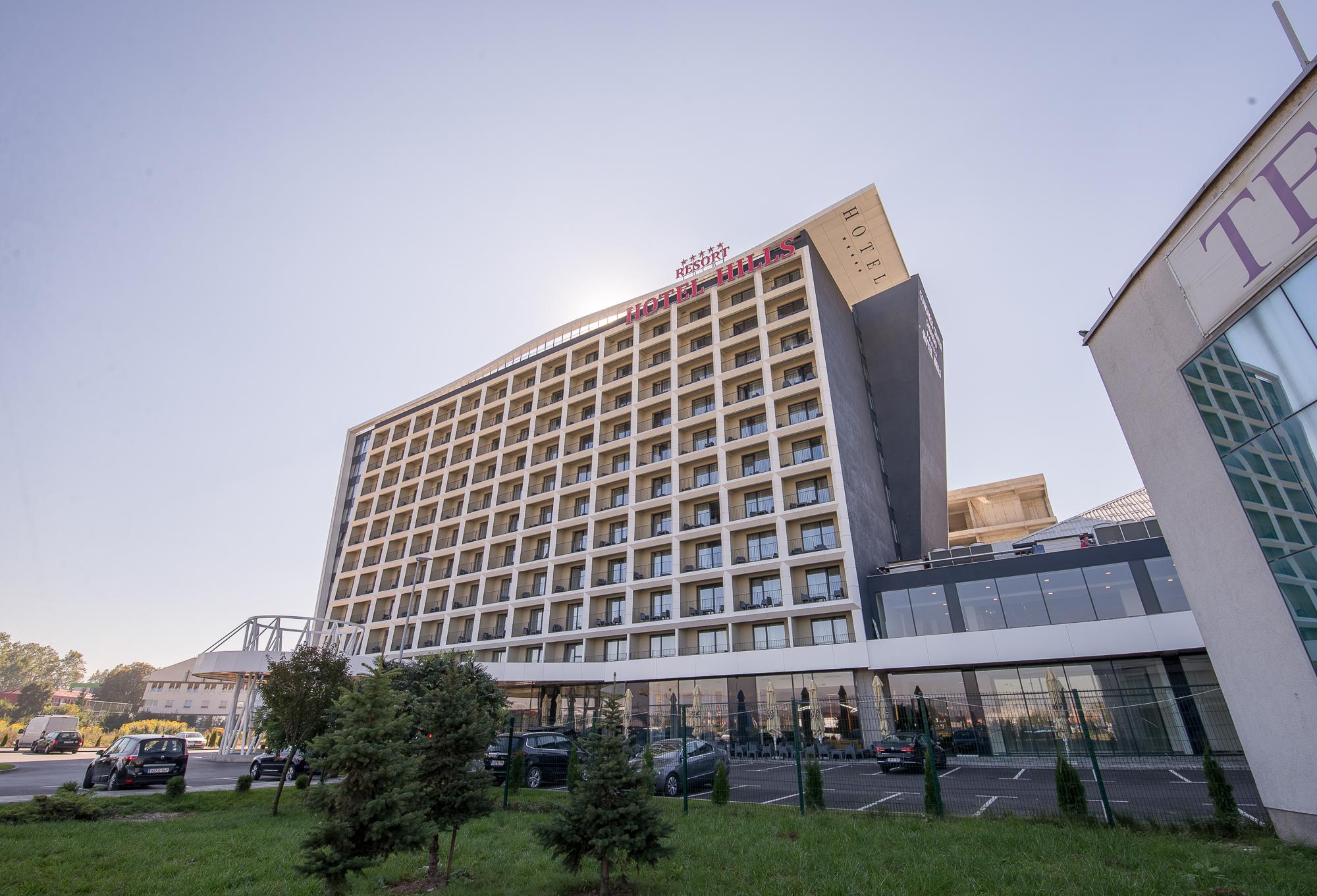 Hotel Hills Sarajevo Congress & Thermal Spa Resort Ilidža Bagian luar foto The photo shows a modern hotel building with multiple floors and a contemporary design. The structure features large windows arranged in a grid pattern and a prominent entrance area at the bottom. There are green areas, possibly with trees or landsca