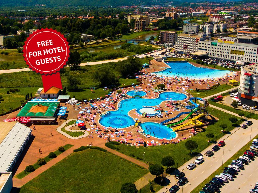 Hotel Hills Sarajevo Congress & Thermal Spa Resort Ilidža Bagian luar foto The photo shows an aerial view of a large swimming pool area, likely part of a hotel or resort. There are several pools of different shapes and sizes, including one that resembles a Mickey Mouse shape. The area is filled with numerous sun loungers an